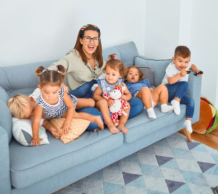 Erzieherin sitzt mit fünf Kindern auf einem blauen Sofa.